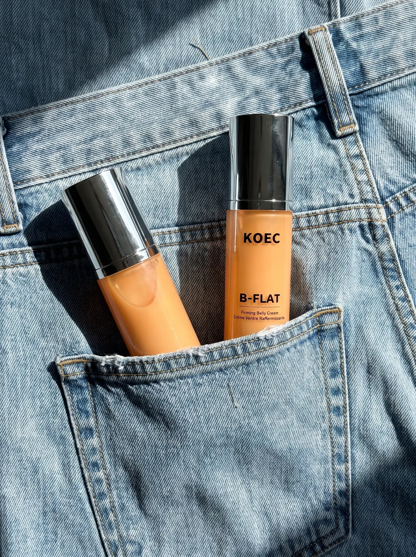 KOEC B-FLAT belly firming cream tucked into the pocket of light-wash denim